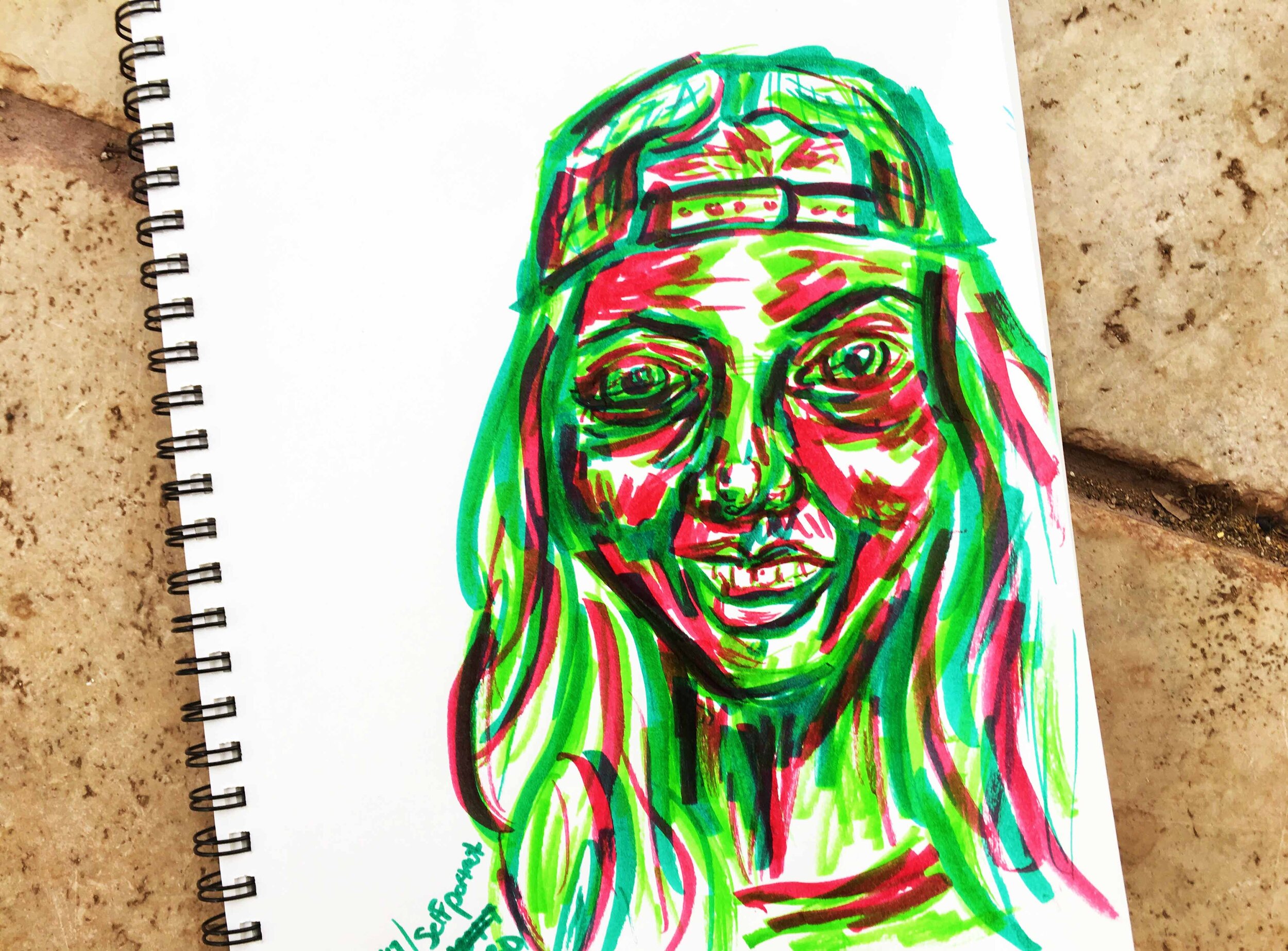 Day 6: photo of a self-portrait wearing a hat using markers sitting on a tile floor.