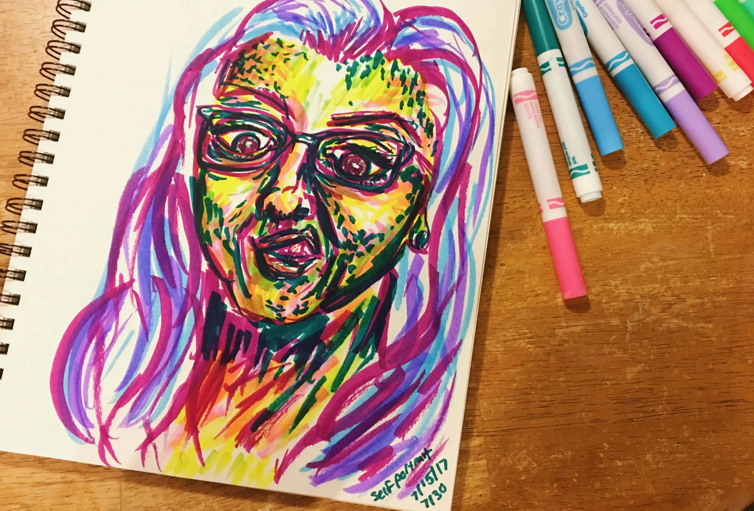 Day 7: photo of a self-portrait wearing glasses and sticking my tongue out surrounded by art supplies on a table.