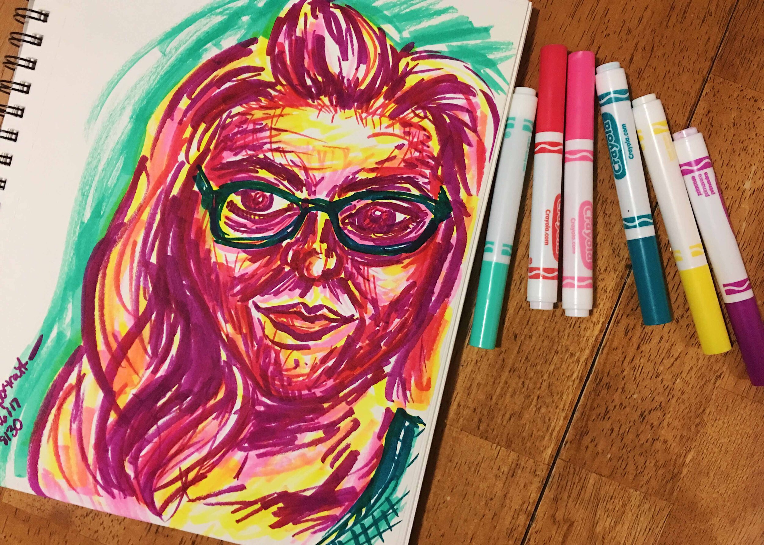 Day 8: photo of a self-portrait wearing glasses and smiling surrounded by art supplies on a table.