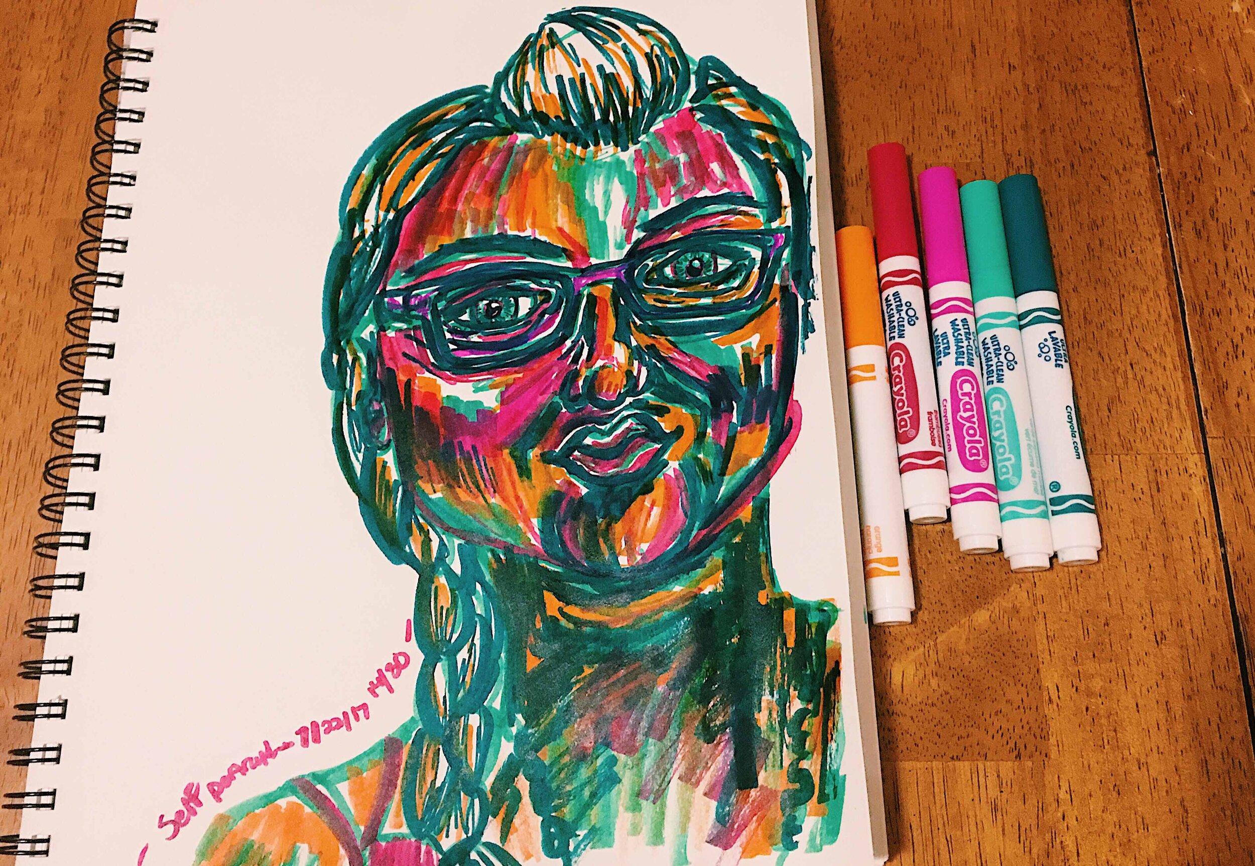 Day 14: photo of a self-portrait wearing glasses and braided hair surrounded by art supplies on a table.