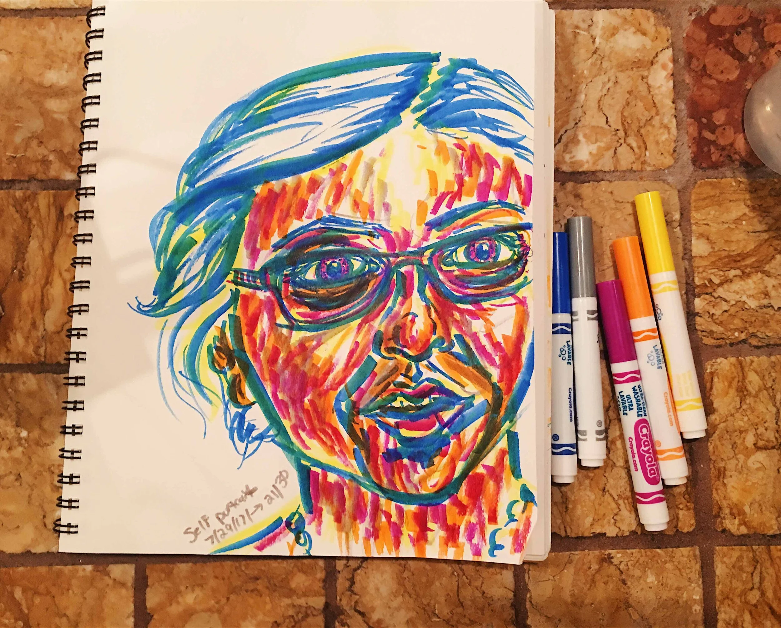 Day 21: photo of a marker self-portrait wearing glasses surrounded by art supplies on a tile counter top.