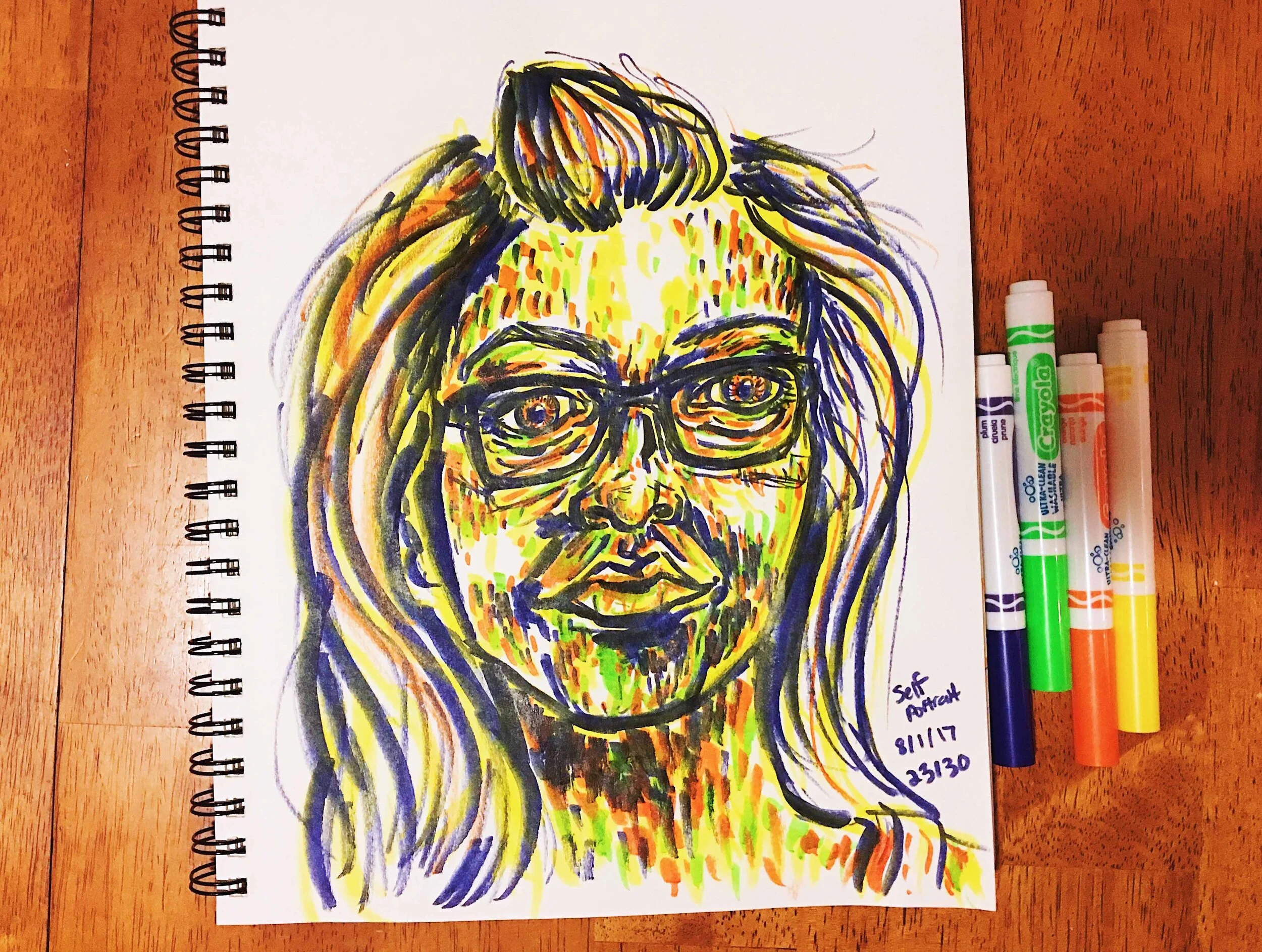 Day 23: photo of a self-portrait wearing glasses surrounded by art supplies on a table.