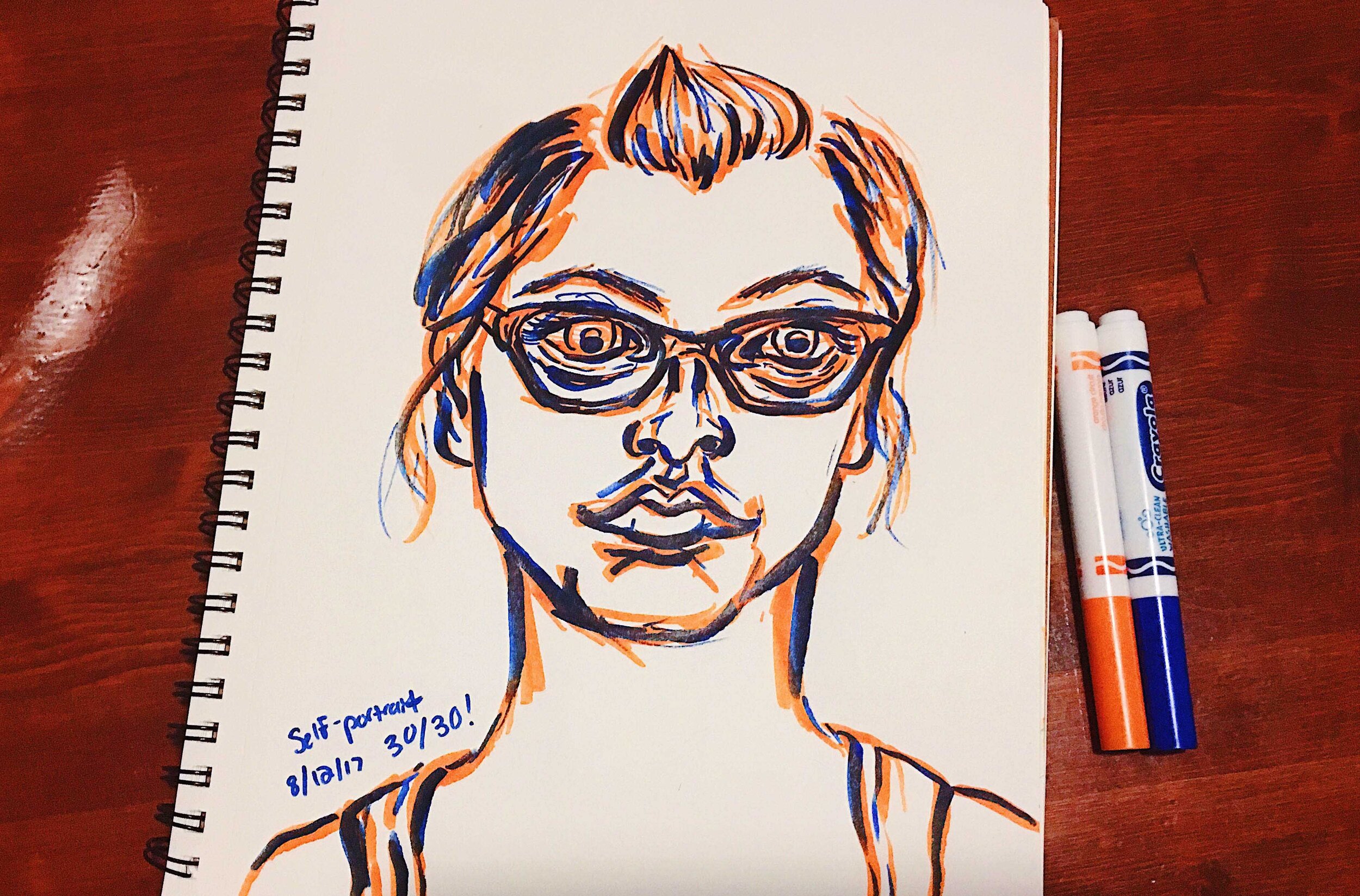 Day 30: photo of a marker self-portrait wearing glasses surrounded by art supplies on a table.