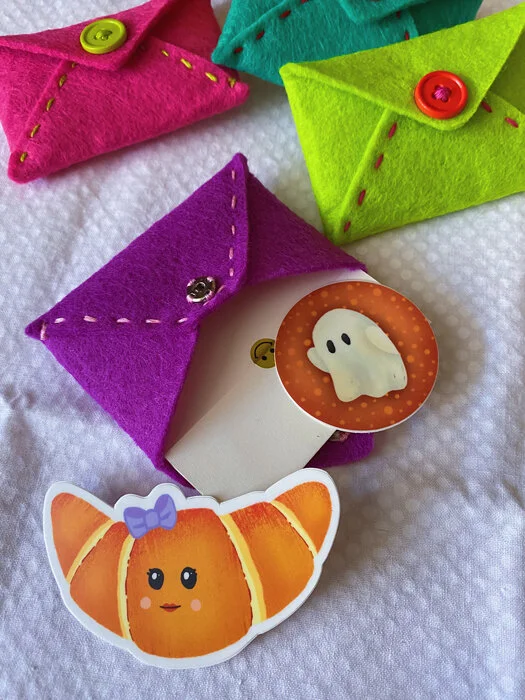 Overview photo showing the back of colorful handmade envelopes made from felt with examples of stickers to fill them with.
