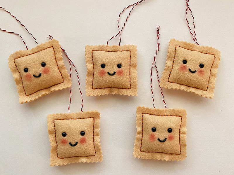Overview photo of hand sewn felt ravioli ornaments on a white background. Each has a happy or sad face with blushing cheeks.