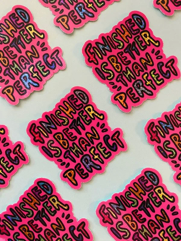 Overview group photo of holographic vinyl stickers that read "finished is better than perfect" set against a blue background.