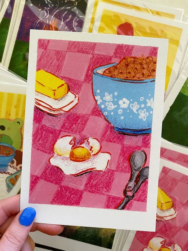 Detail of a broken egg on a pink tablecloth with butter and blue bowl. Print measures 5" by 7" and is on recycled stock.
