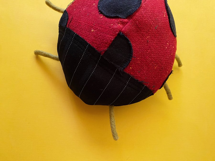 Close up photo of a handmade ladybug plushie made out of recycled fabrics on a yellow background.