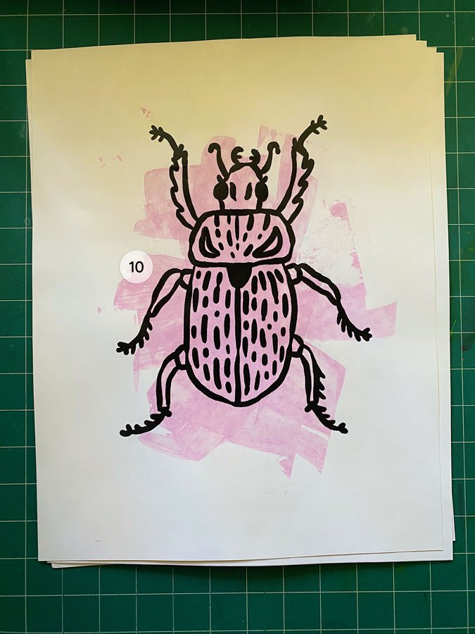 Overview of a hand made 11"x14" screen print of a beetle with a colorful purple paint swipe background.