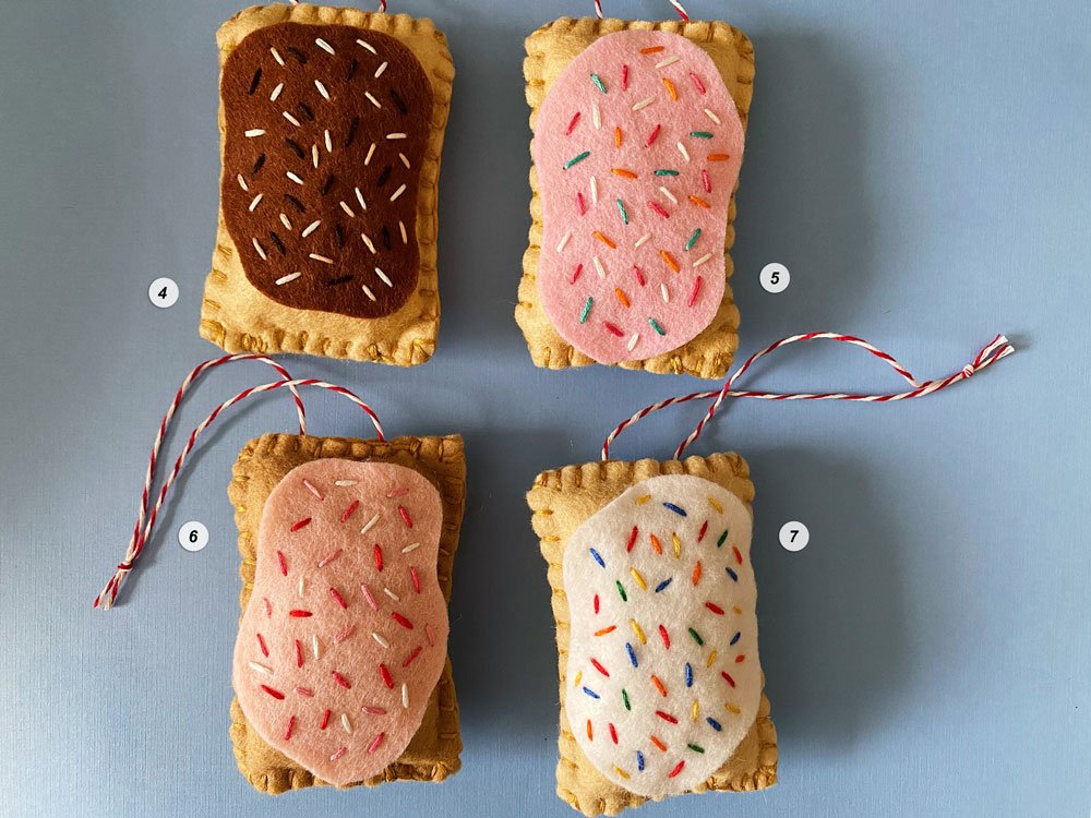 Photo of four colorful hand-sewn and embroidered felt pop tart ornaments on a blue background.