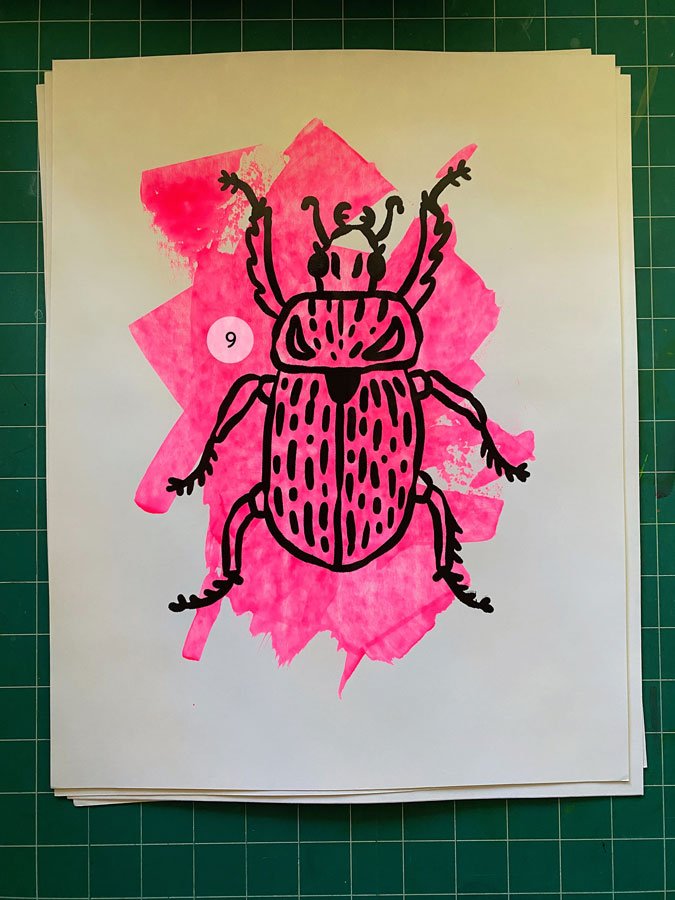 Overview of a hand made 11"x14" screen print of a beetle with a colorful neon pink paint swipe background.
