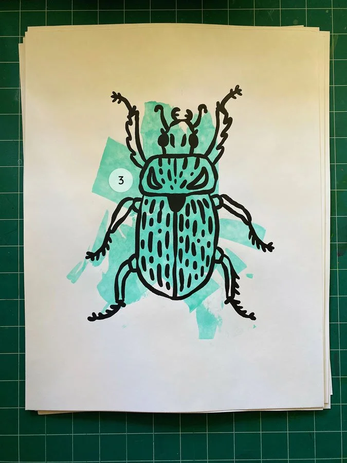 Overview of a hand made 11"x14" screen print of a beetle with a colorful blue paint swipe background.