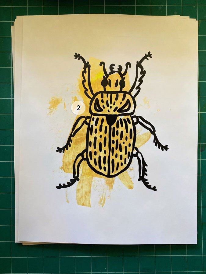Overview of a hand made 11"x14" screen print of a beetle with a colorful gold paint swipe background.