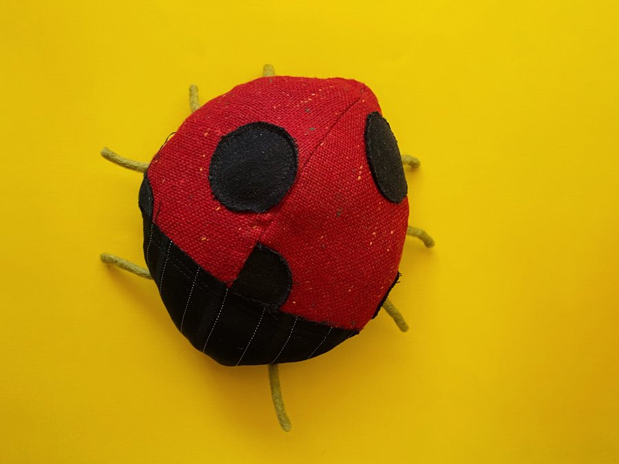 Overview photo of a handmade ladybug plushie made out of recycled fabrics on a yellow background.