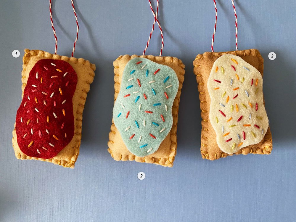 Photo of three colorful hand-sewn and embroidered felt pop tart ornaments on a blue background.