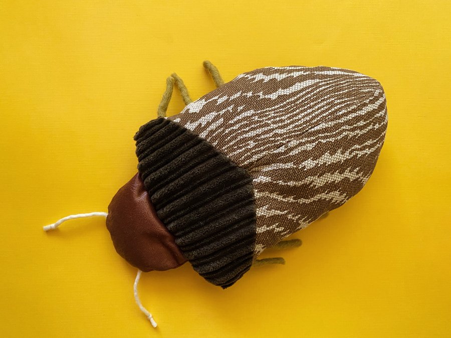 Overview photo of a handmade shield bug plushie made out of recycled fabrics on a yellow background.