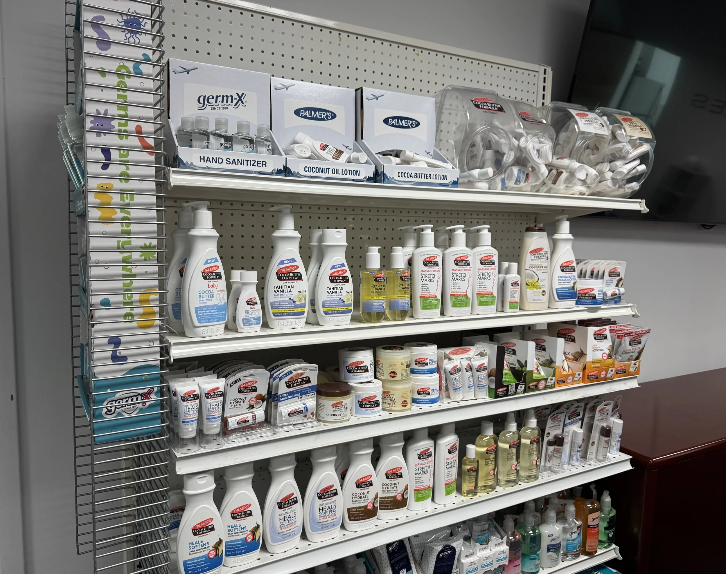 Retail shelf displays hand sanitizers, lotions, and skin care products, including brands like Palmer's, with bottles, tubes, and small jars organized on white shelves.