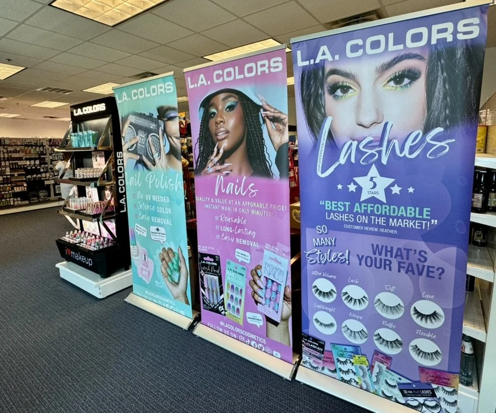 Display banners showcasing L.A. Colors beauty products, including nail polish, eyelashes, and lash styles, in a retail store aisle.