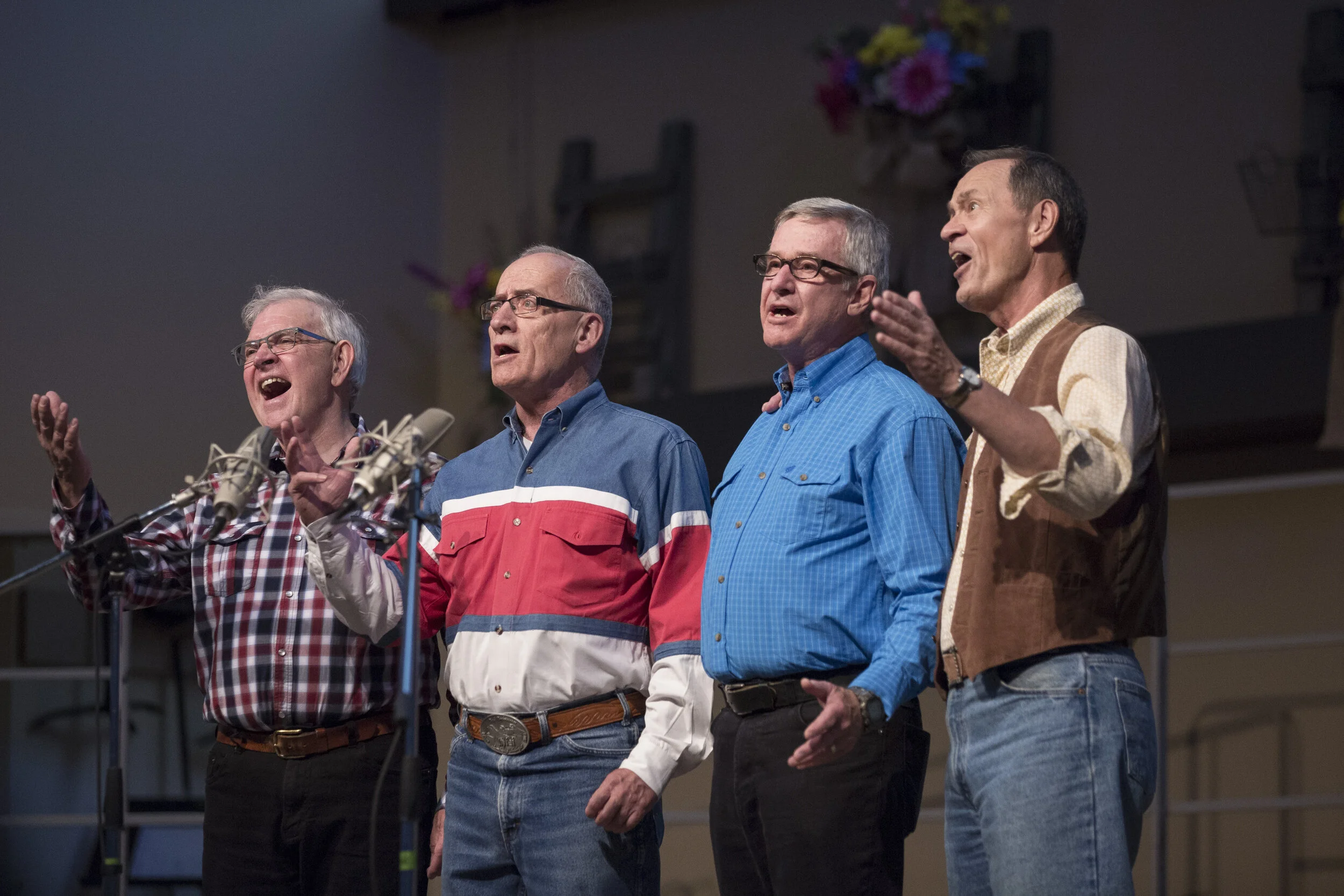 Four singers in a barbershop quartet performing onstage, wearing various Western garb.