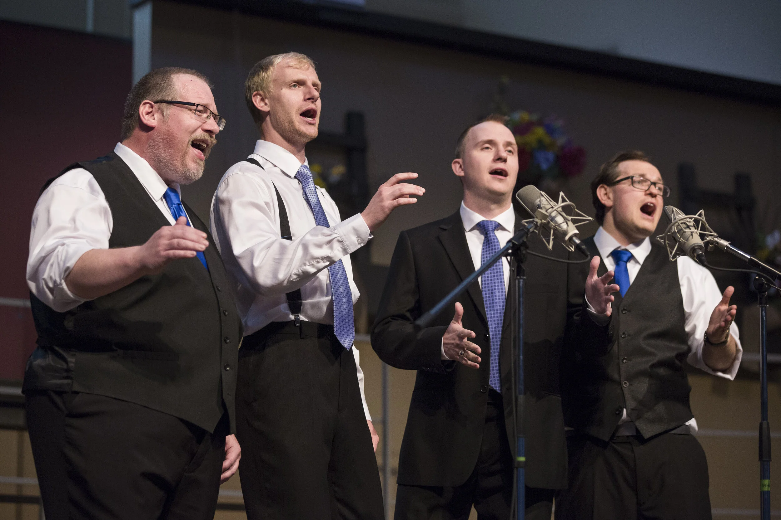 Four singers in a barbershop quartet performing onstage in various formal attire.