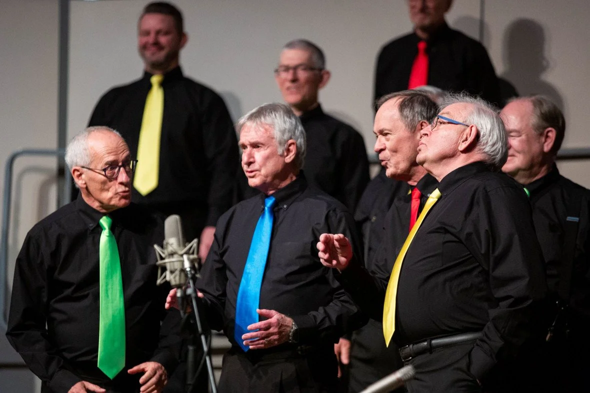 Forever Glad, a four-man barbershop quartet, performing onstage in black shirts with neon coloured ties.
