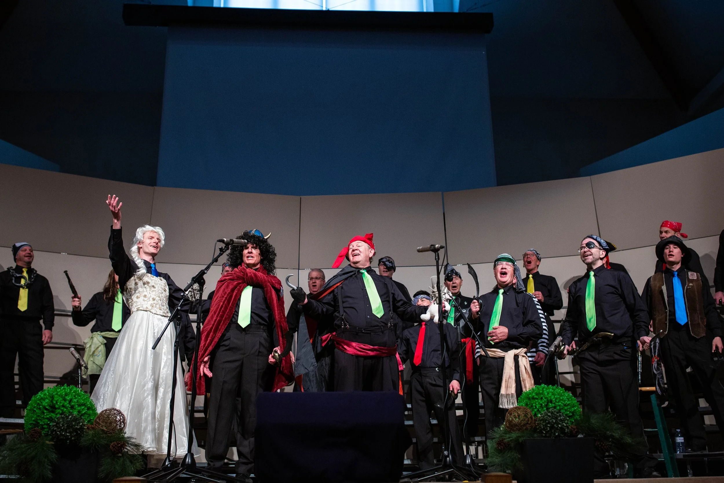 Photo of Acappella Road in performance, wearing black outfits, colourful ties, and various pirate-themed accessories like eyepatches and headbands during a Peter Pan-themed number.