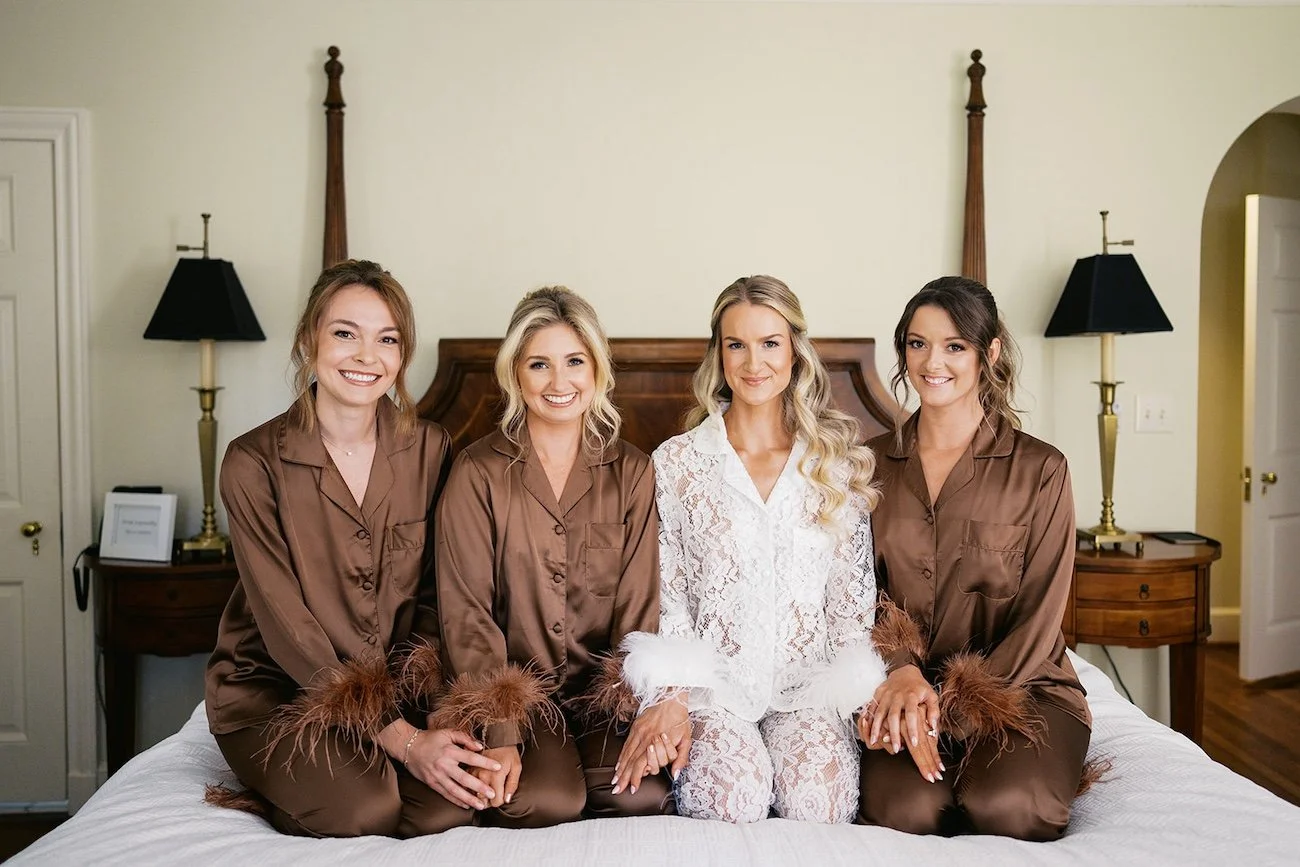 bride and wedding party pose together on top of the bed in their pjs