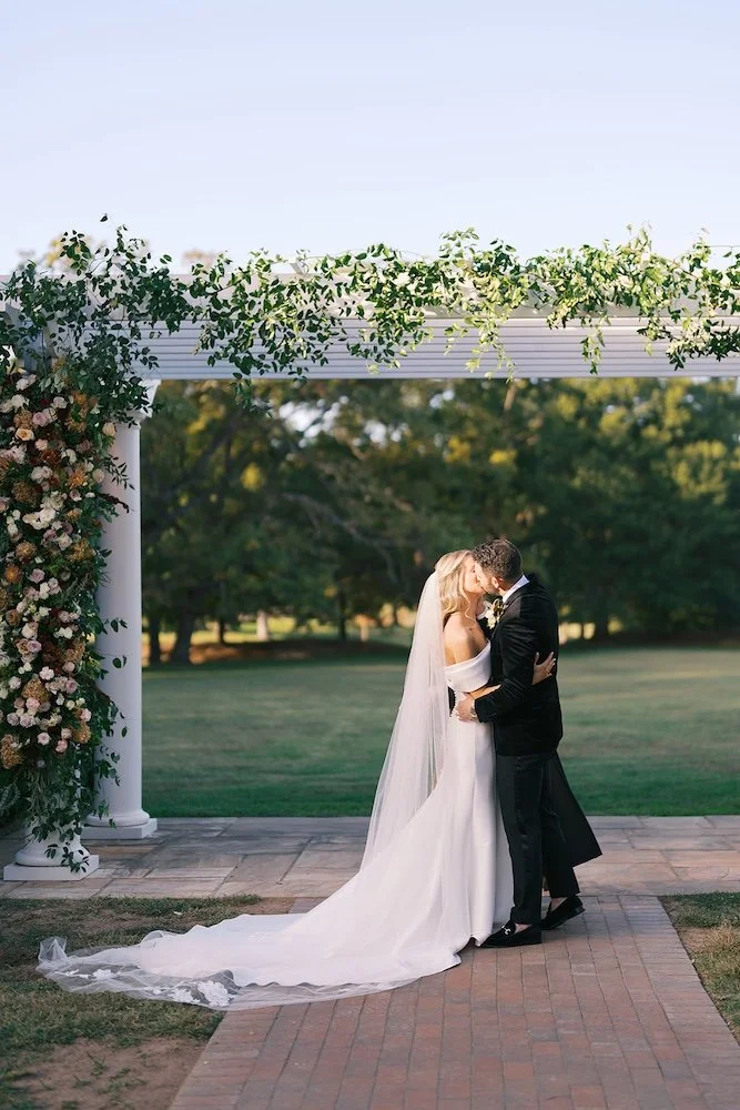 bride and groom first kiss in front of their ceremony floral arch