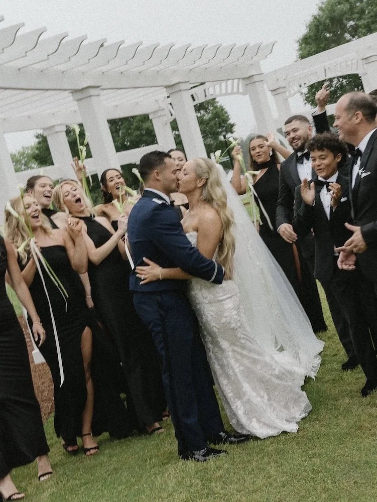 bride and groom standing up kissing with the wedding party cheering them on