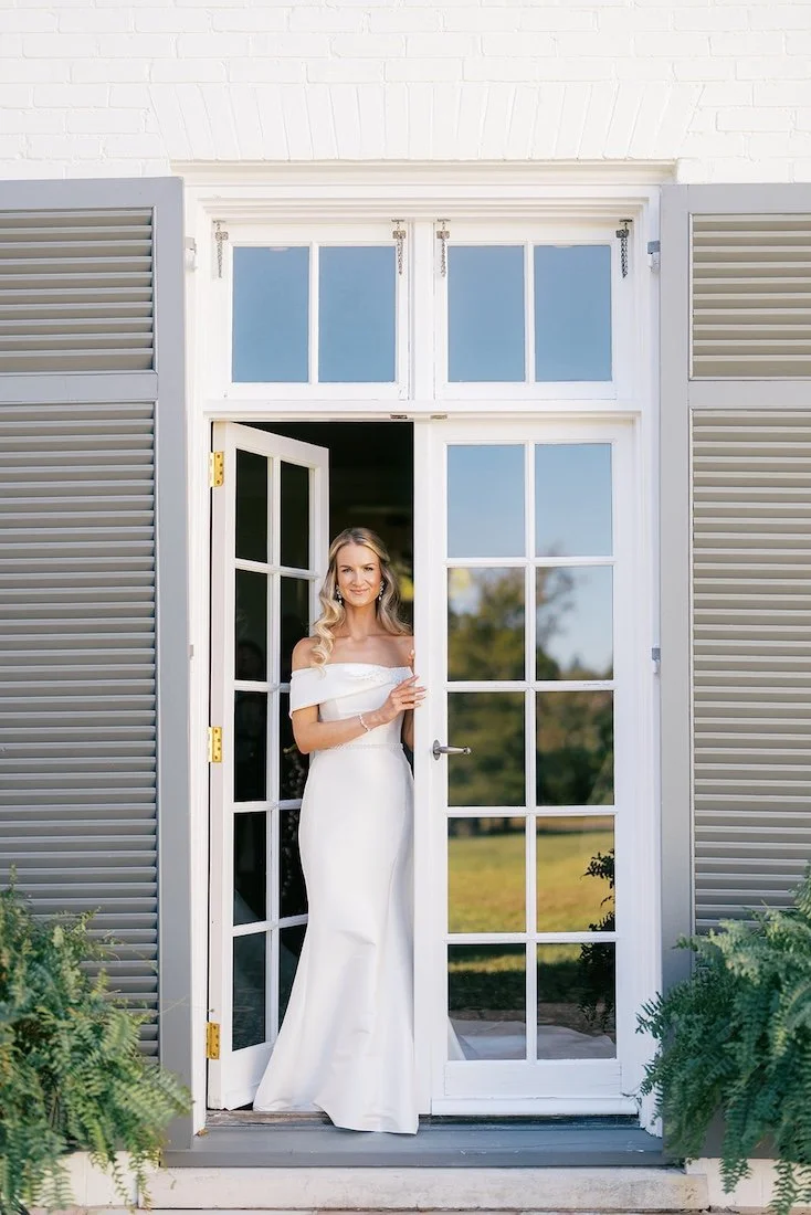 elegant bride with glam waves standing outside boxwood estate in a white wedding dress