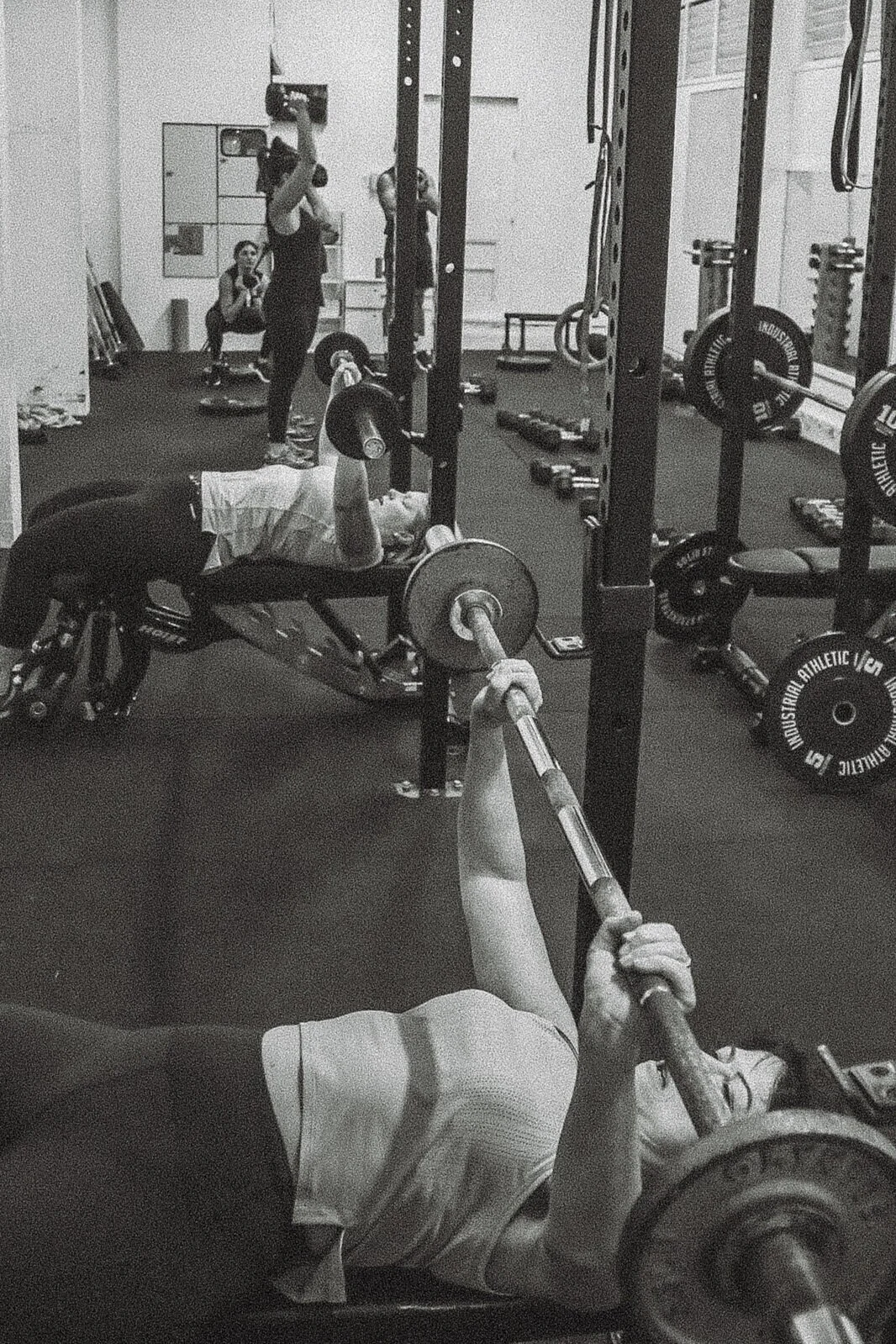 Serious active slim young ethnic female wearing green top and dark leggings with sneakers looking at camera near kettlebell on light grey background