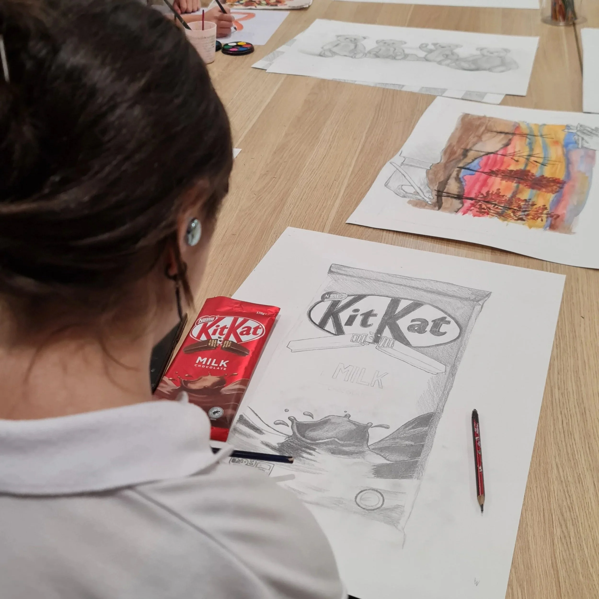 Children at a table coloring and drawing pictures of trees, landscapes, and graphics related to Kit Kat chocolate.