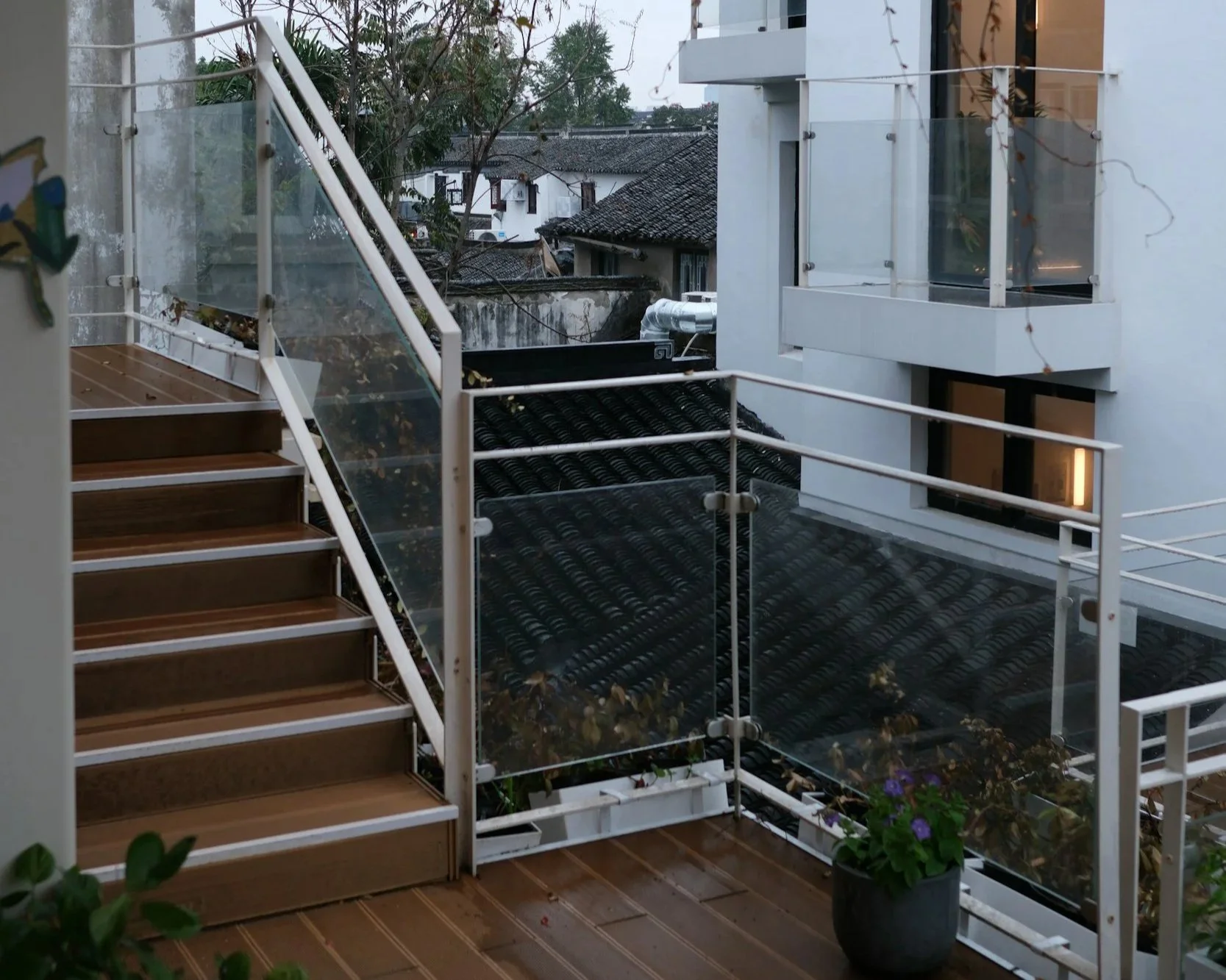 Modern outdoor staircase with wood-effect composite treads, white powder-coated metal stringers, and tempered glass balustrade panels with stainless steel clamps.