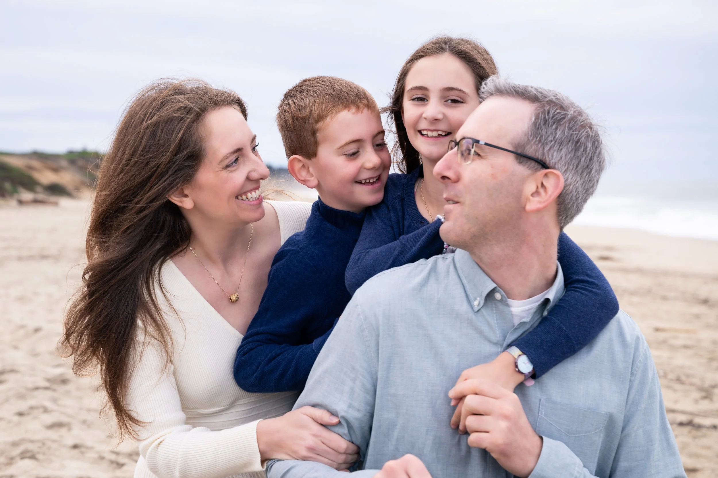 A close-up family portrait at Half Moon Bay featuring parents and children smiling and embracing during a beach session.