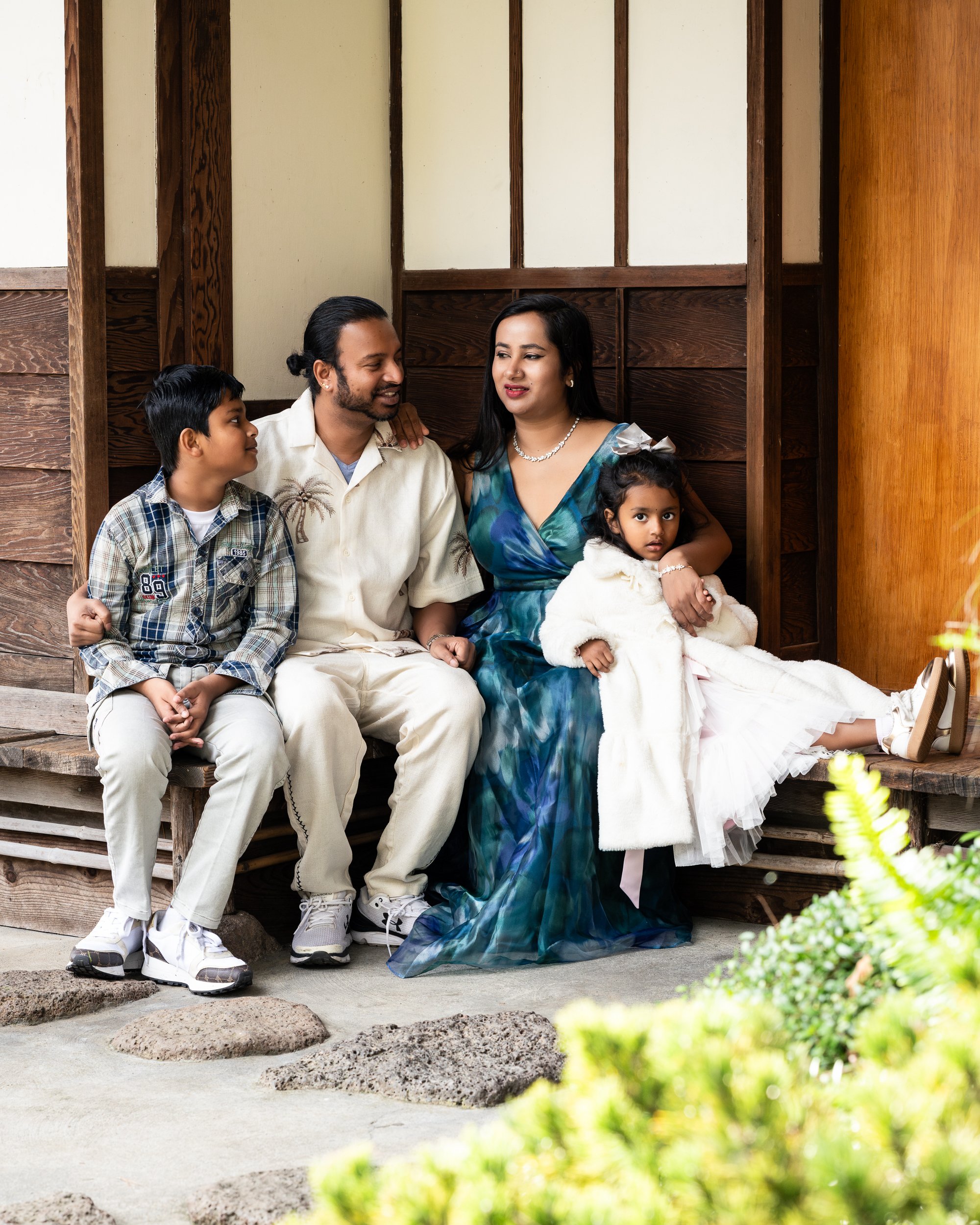 A family sits closely together during a Give Light free family photography session at the San Mateo Japanese Garden, capturing a calm, intimate moment surrounded by natural wood textures and soft light.