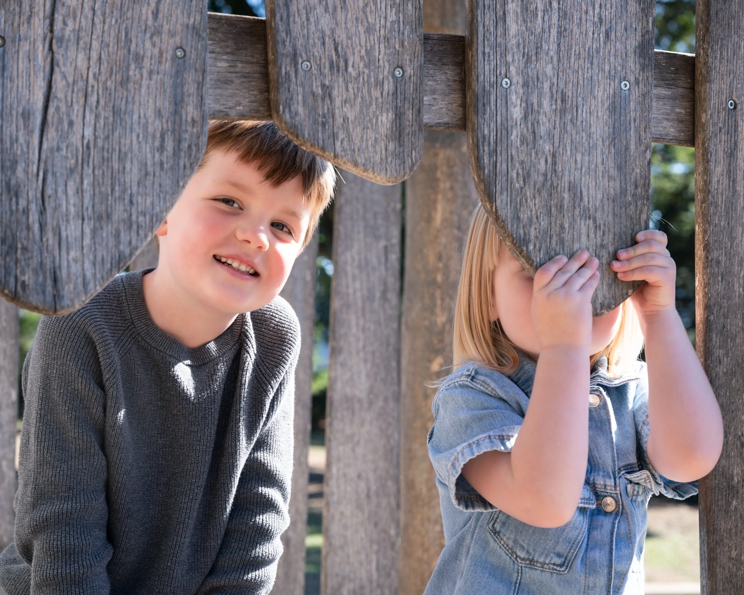 Two young children photographed in natural light at a playground, capturing playful and candid expressions.
