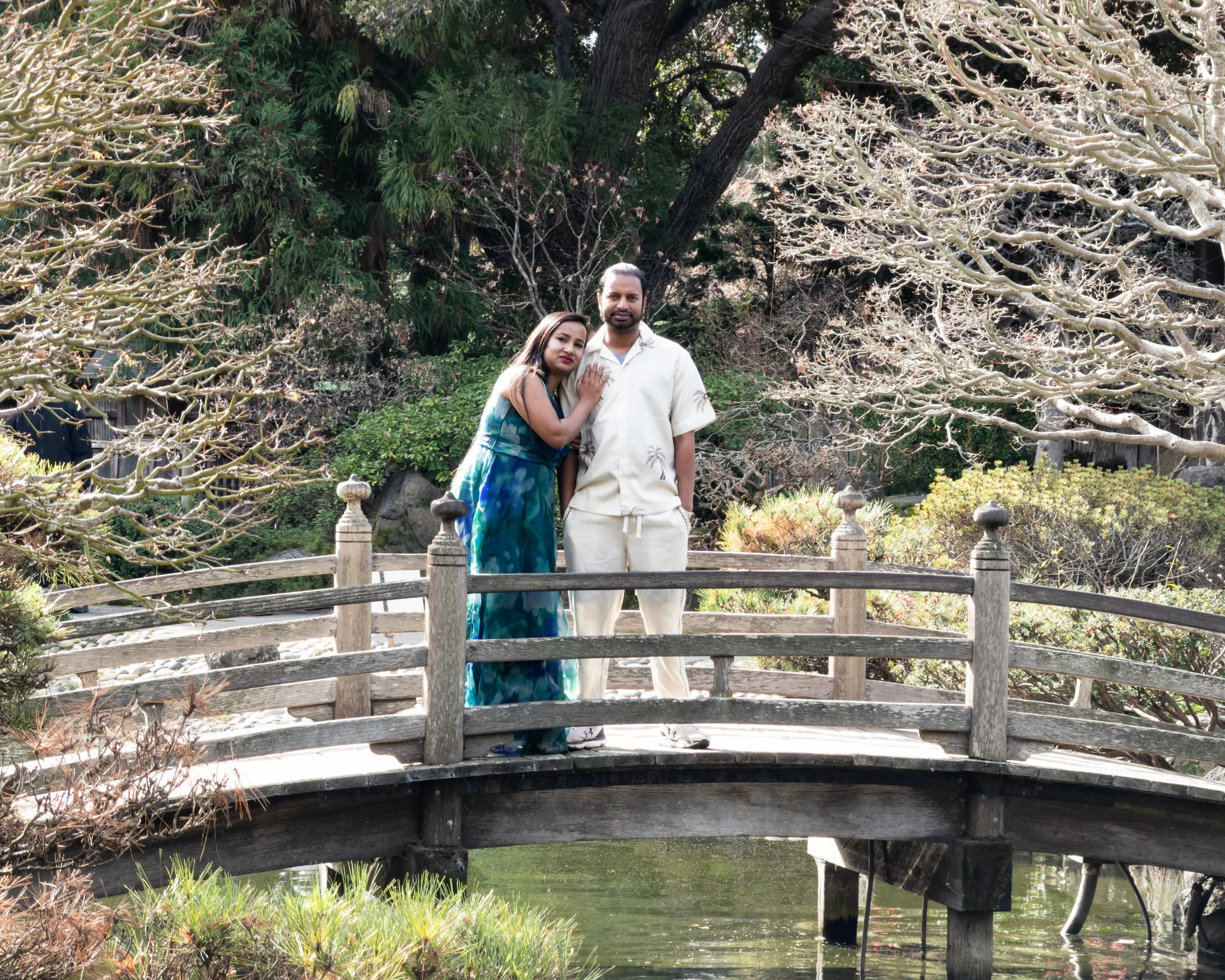 Parents stand together on a garden bridge during a Give Light family photo session at the San Mateo Japanese Garden, emphasizing connection, presence, and simplicity.