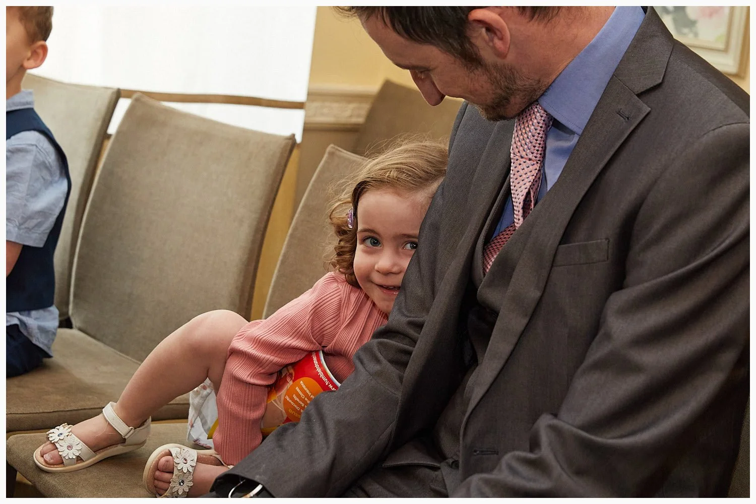 A shy little girl peeps out from behind her dad during the wedding at Basingstoke Register Office