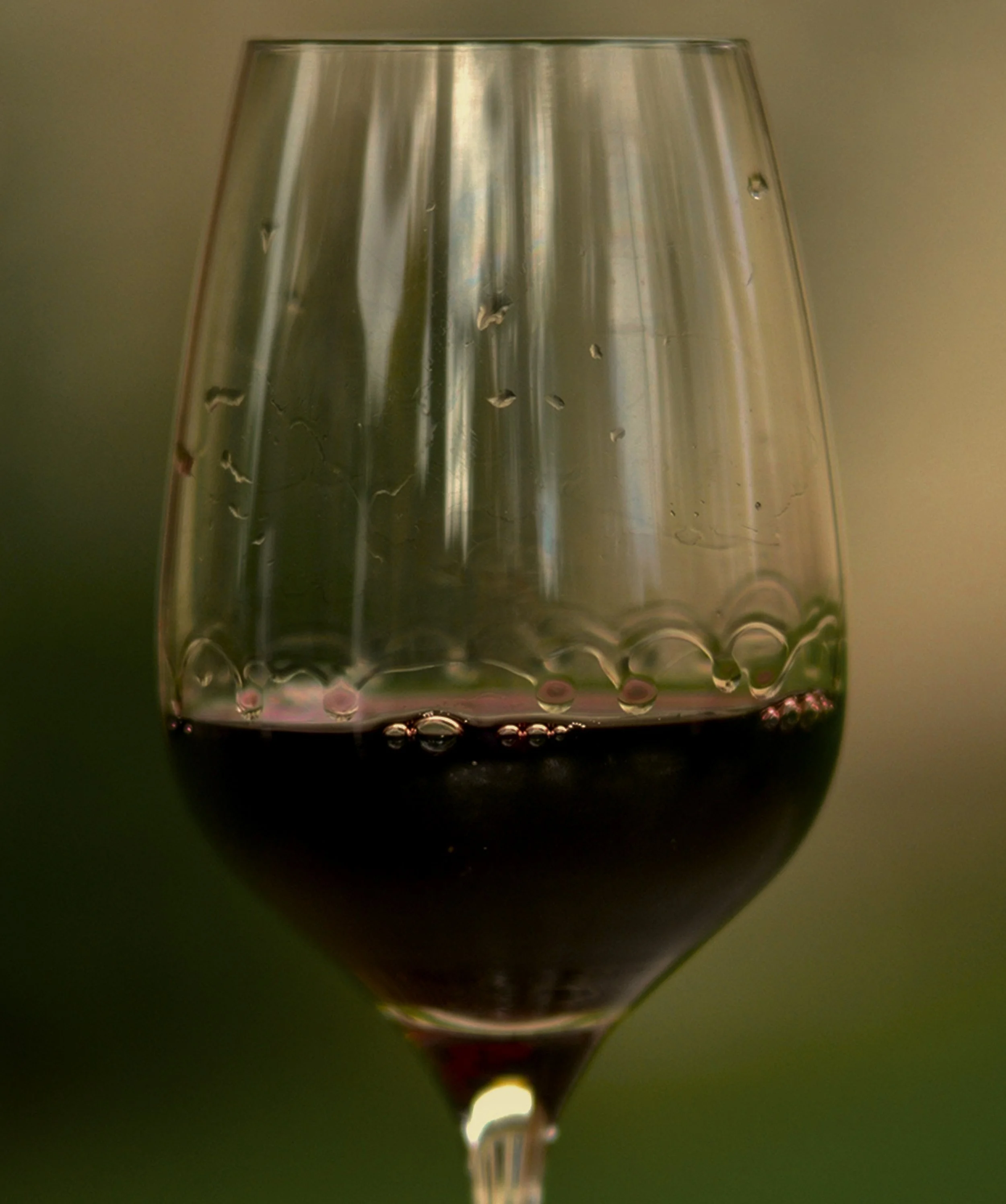 Glass of red wine, half full, against a blurred background.