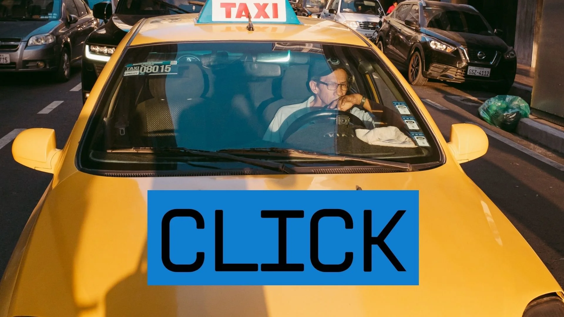 Taxista en un taxi amarillo en un estacionamiento, con un cartel que dice 'TAXI' en el techo del vehículo, y un letrero en la parte frontal que dice 'CLICK'.