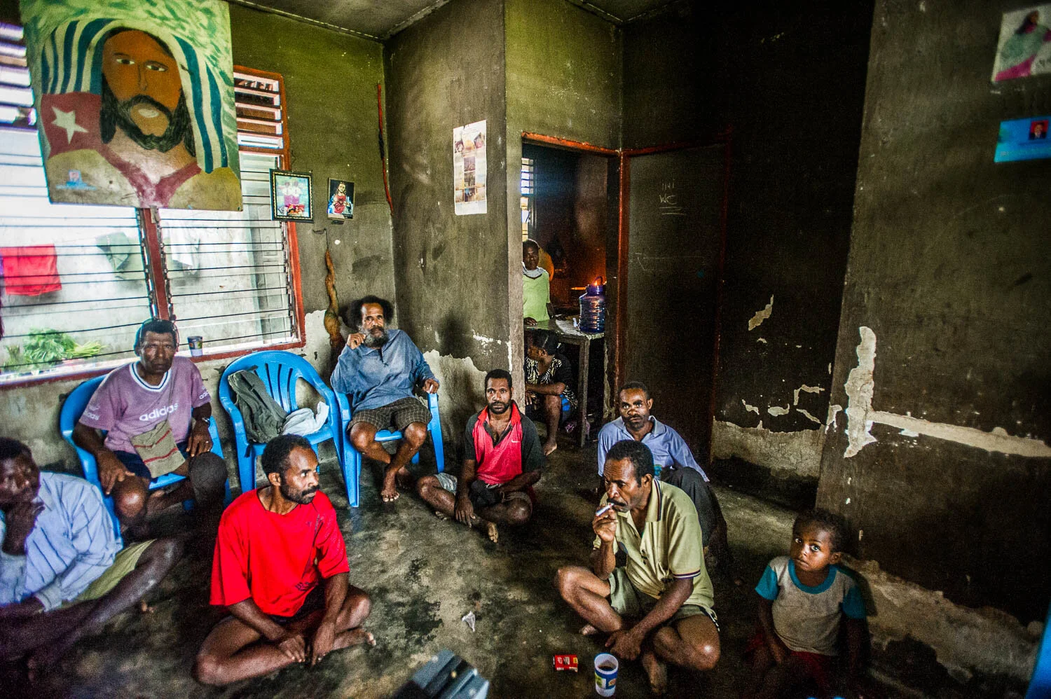 Members of the Free Papuan Movement in Klamono village smoke cigarettes under a painting of Jesus wearing a West Papuan Morning Star flag.