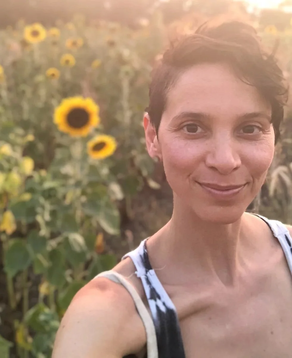 Person taking a selfie in a sunflower field during sunset.