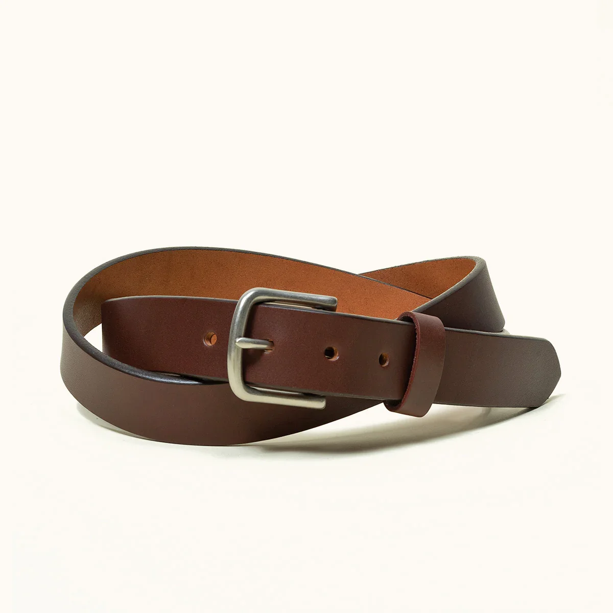 Brown leather belt with a silver buckle, coiled on a plain white background.