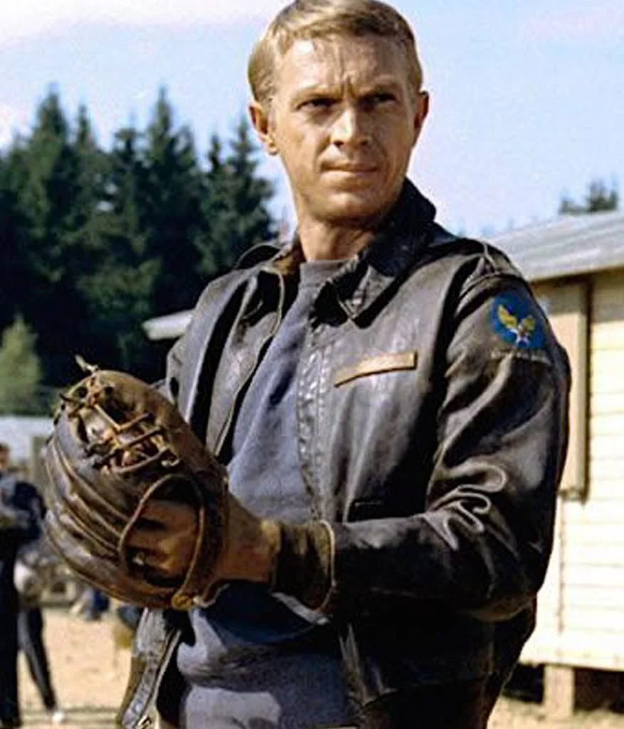 A man in a vintage leather baseball glove and a leather bomber jacket standing outdoors, with trees and a building in the background.
