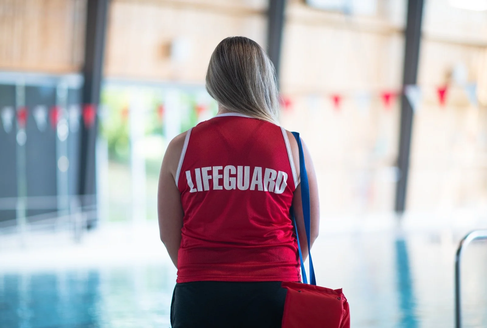 The back of a young woman lifeguard wearing a "Lifeguard" tank-top at a swimming pool