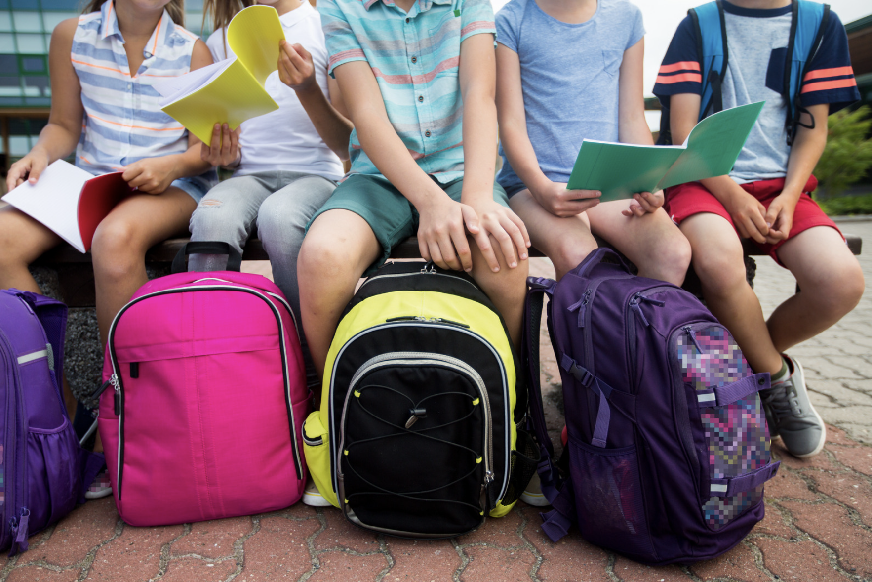 Image of kids sitting with large backpacks in front of them.