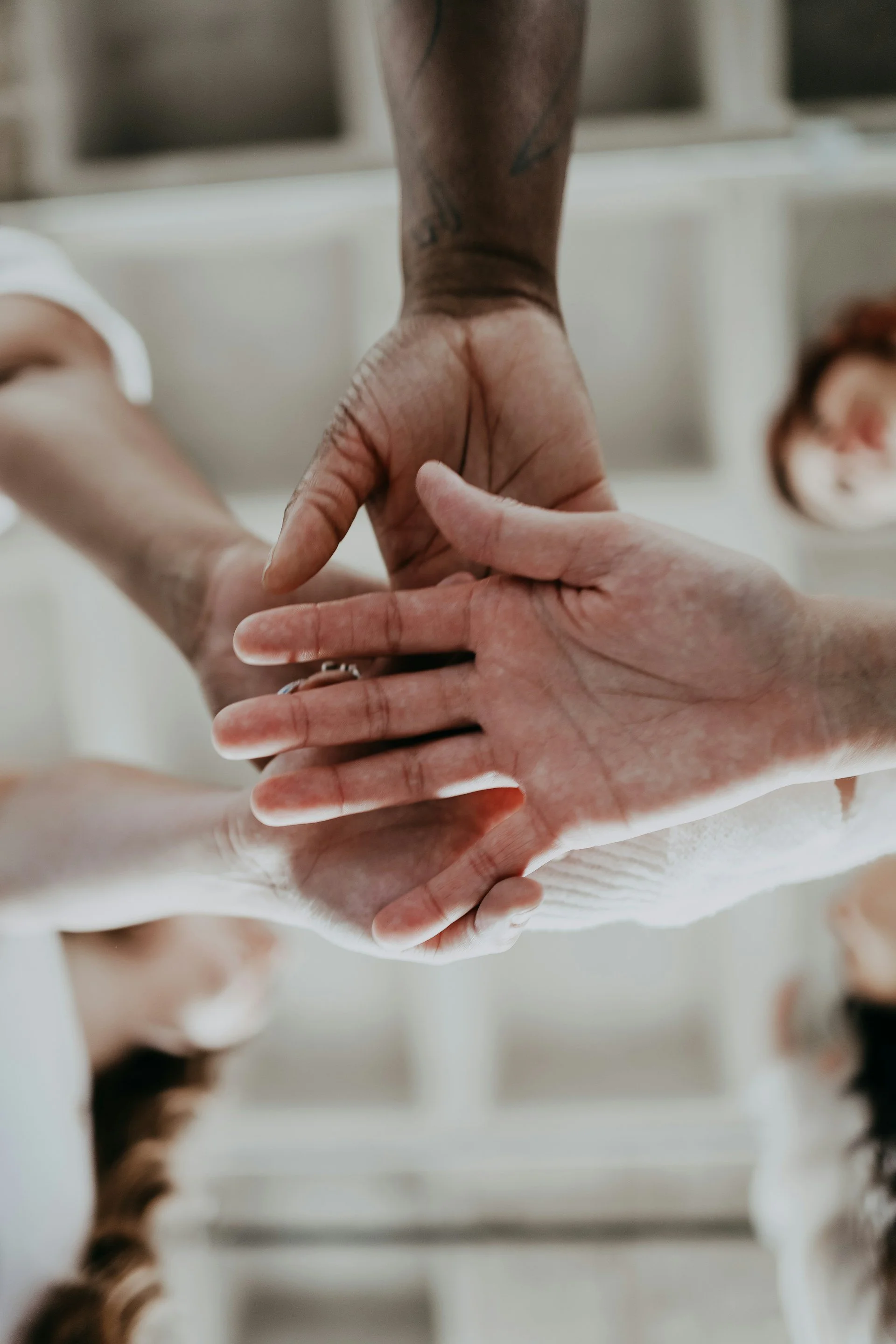 Close-up of multiple hands stacked together in a gesture of unity or teamwork, with a blurred background of a person with brown hair.