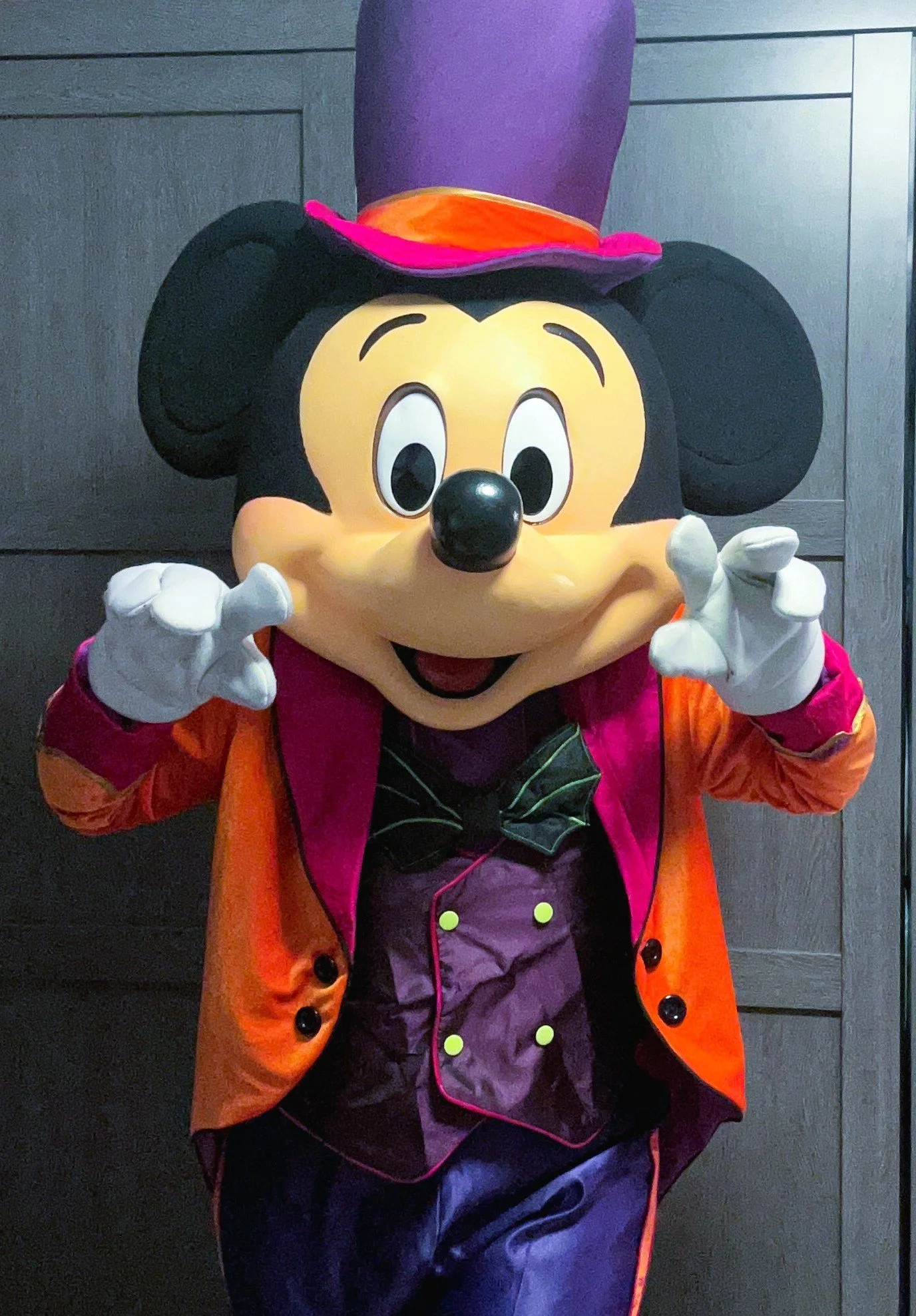 Mr. Mouse party character dressed as a Halloween magician, wearing a colorful hat and a festive orange and purple outfit, with a dark background.