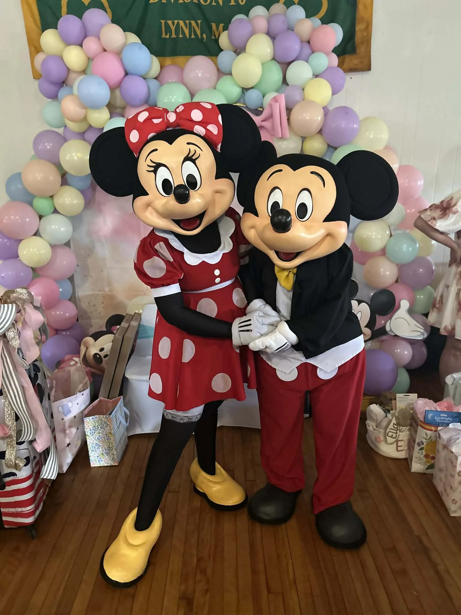 Mr and Miss Mouse party characters hugging in front of a colorful balloon backdrop at a celebration or party.