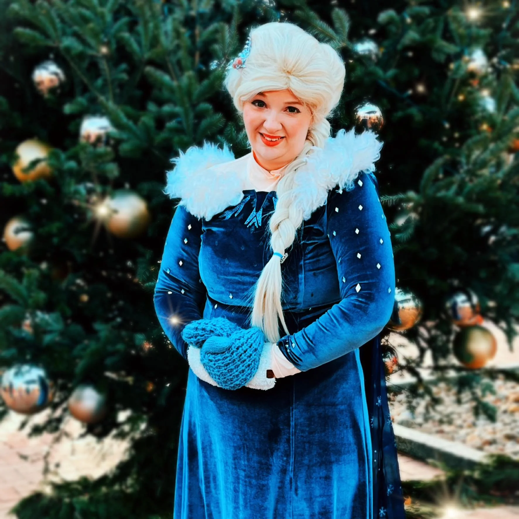 Snow Queen party princess standing in front of a decorated Christmas tree, smiling at the camera.